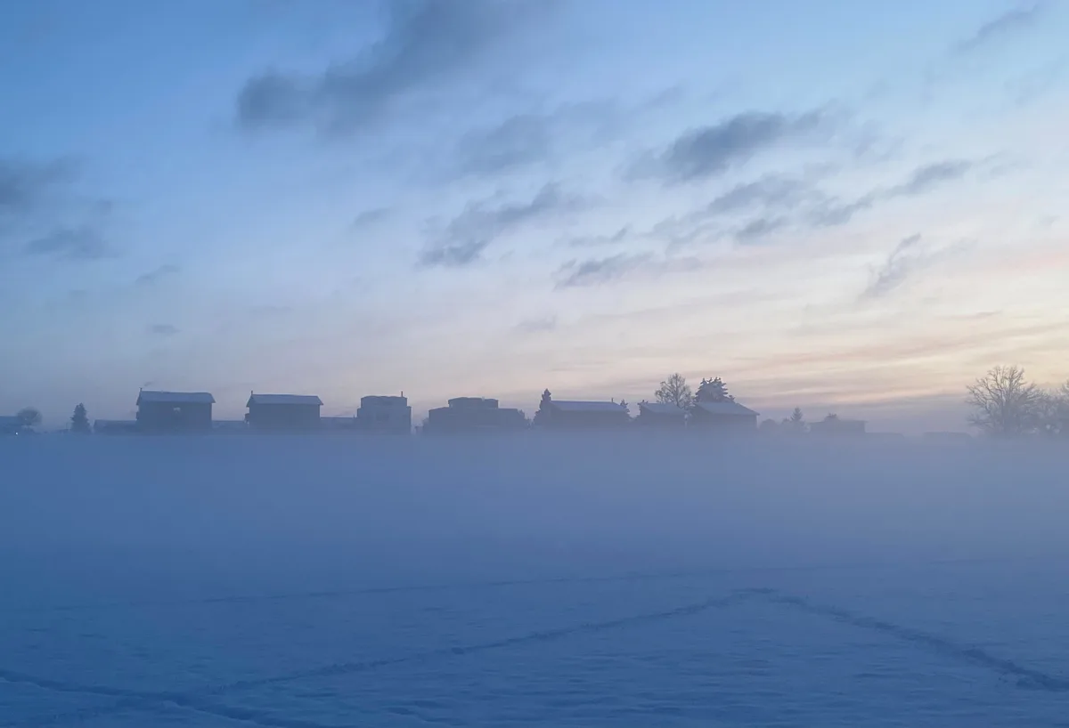 Ein eisiger Wind wehte am Abend des 11. Januar im Tanner Ried. Schneelandschaft, Häuser im Hintergrund und etwas Nebel im Abendlicht